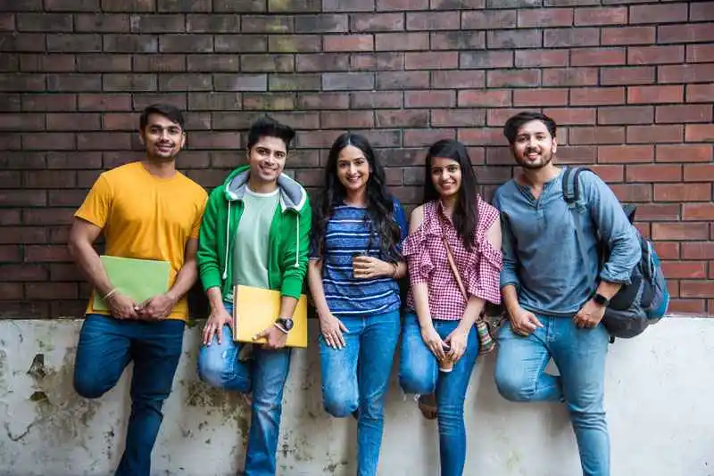 A few students are standing outside the university with their bags and files