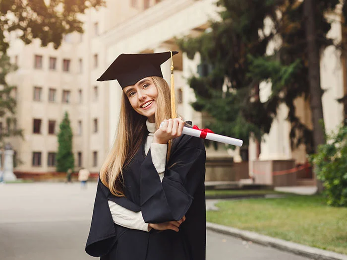 A female student is standing in front of the college building holding her graduation certificate